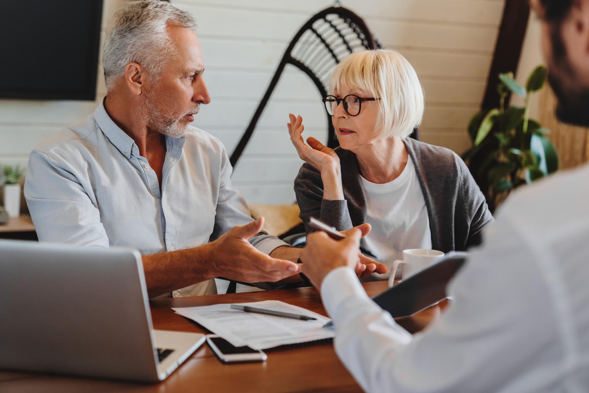 Financial advisor giving retirement advice to old couple while they arguing at home interior